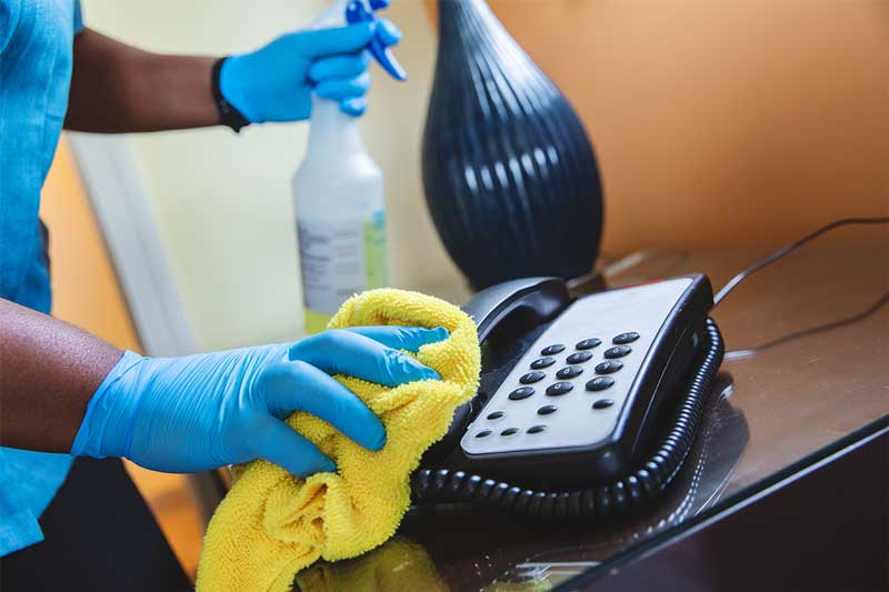 Person with spray bottle and yellow cloth wiping clean telephone at resort